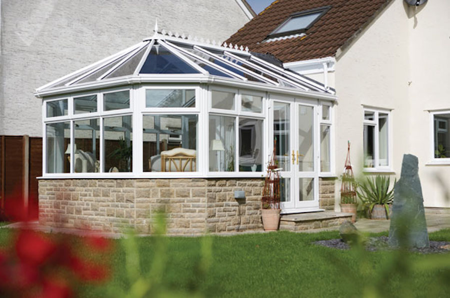 White Victorian conservatory with a stone base attached to a house in Aspley Heath, overlooking a garden.