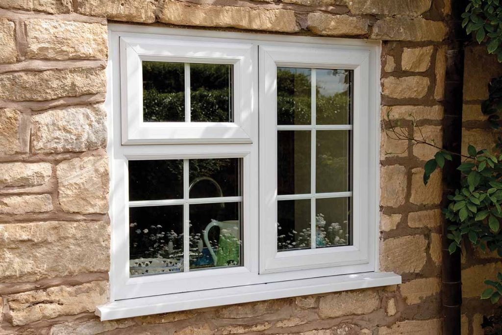 White double window with multiple panes set in a rustic stone wall of a cottage.