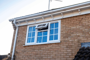 White uPVC window with top opening pane on brick house exterior, with roof antenna visible.