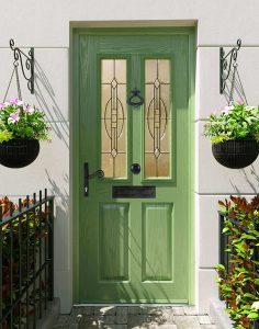 A green composite front door with two decorative glass panels, complemented by hanging flower baskets on either side.